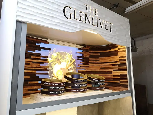 A Glenlivet display bay with a curved white canopy, timber slats and a lit bottle plinth